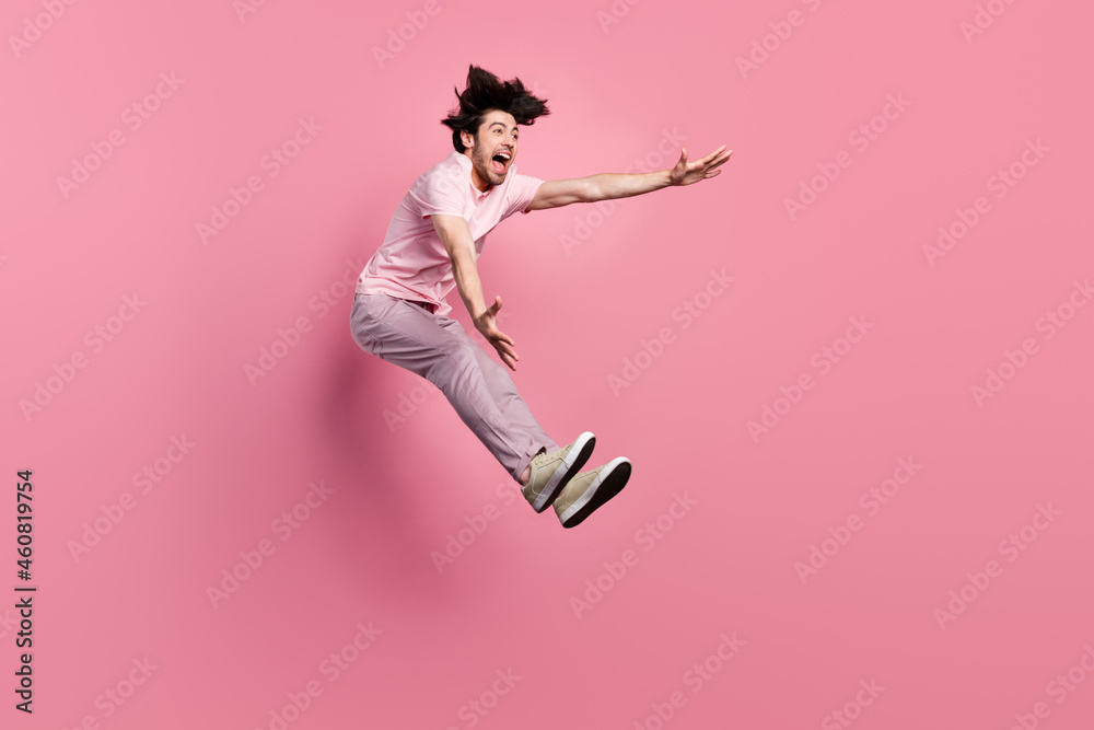 Full size profile side photo of young man amazed excited happy smile jump wind blow catch isolated over pink color background