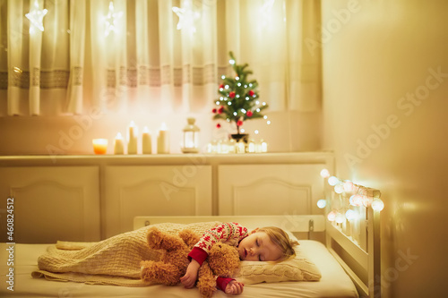 Adorable toddler girl sleeping with her teddy bear under the Christmas tree