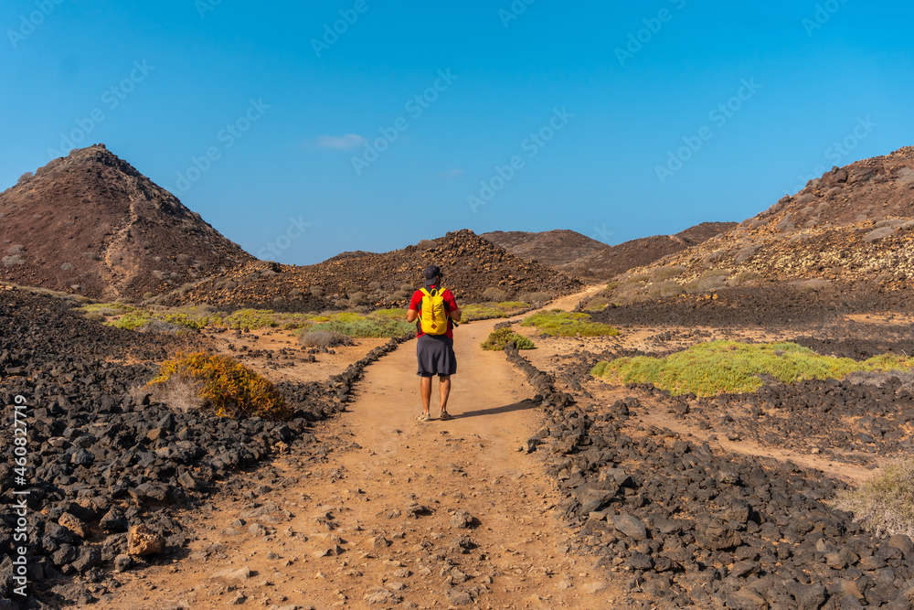 A young man with a yellow backpack on the trail heading north to Isla de Lobos, along the north coast of the island of Fuerteventura, Canary Islands. Spain