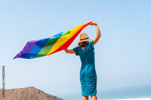 Lgbt symbol  a lesbian person with a green dress and a white hat with the rainbow flag by the sea  symbol of homosexuality