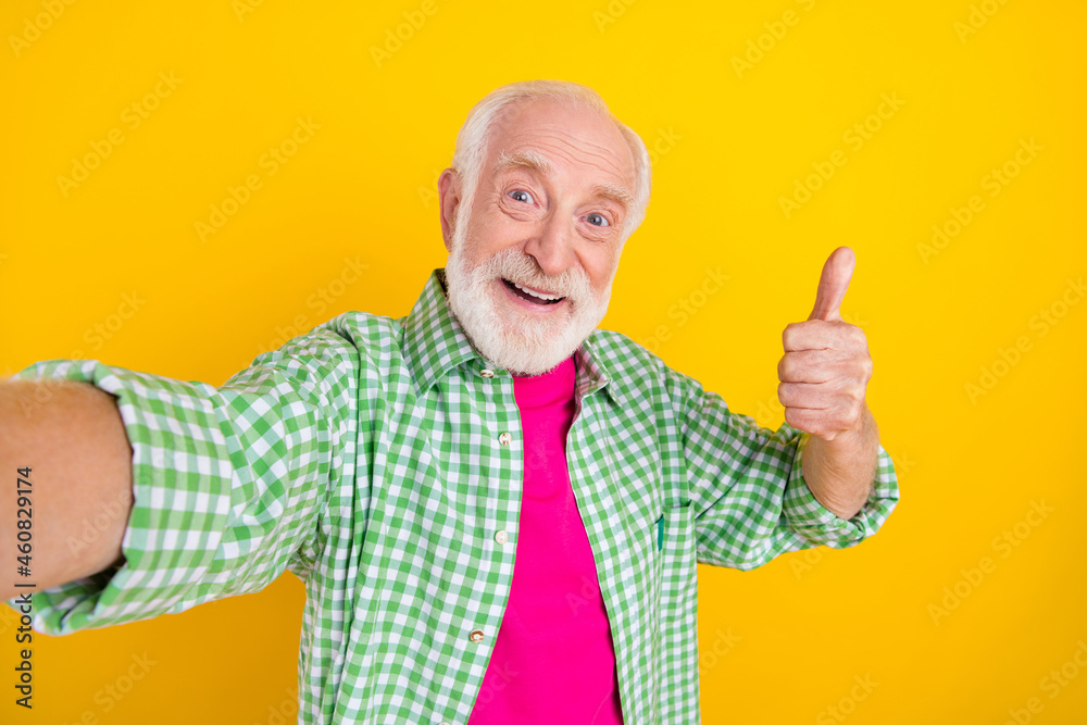Self-portrait of attractive cheerful grey-haired man thumbup advert isolated over bright yellow color background Self-portrait of attractive cheerful grey-haired man thumbup advert isolated over bright yellow color background
