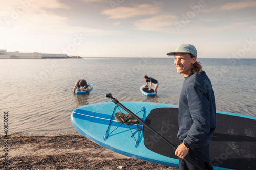 Male instructor carrying paddleboard at beach during sunset