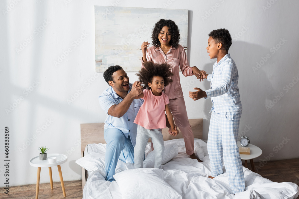 excited african american family in pajamas holding hands while fooling around on bed excited african american family in pajamas holding hands while fooling around on bed