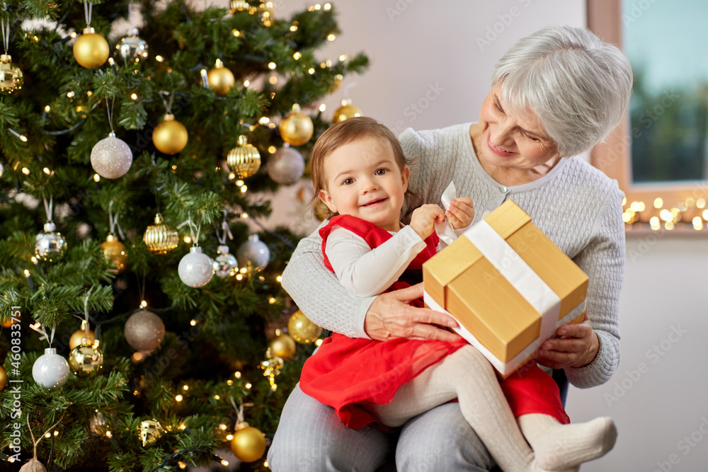 christmas, holidays and family concept - happy grandmother and baby granddaughter with gift at home christmas, holidays and family concept - happy grandmother and baby granddaughter with gift at home
