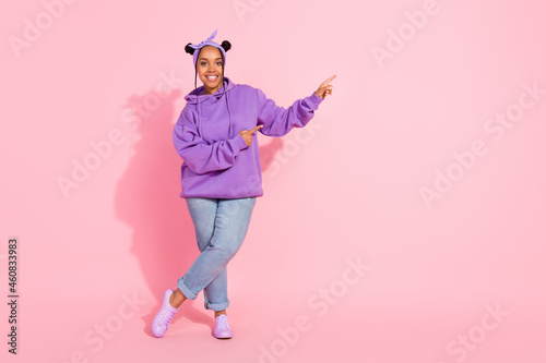 Photo of pretty sweet afro woman wear purple hoodie buns pointing fingers empty space smiling isolated pink color background