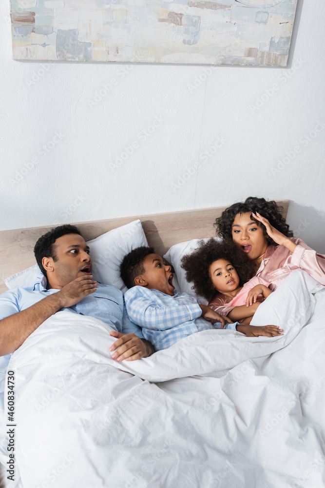 overslept and shocked african american couple lying with kids in bed overslept and shocked african american couple lying with kids in bed