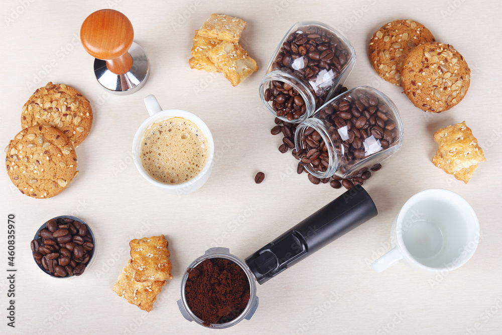Cup of coffee, crackers, cookies, holder with ground coffee, tamper and cans of coffee beans on table. View from above. Cup of coffee, crackers, cookies, holder with ground coffee, tamper and cans of coffee beans on table. View from above.