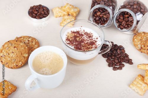 Cup of espresso, cappuccino with chocolate crumbs, cookies, crackers and coffee beans on table.