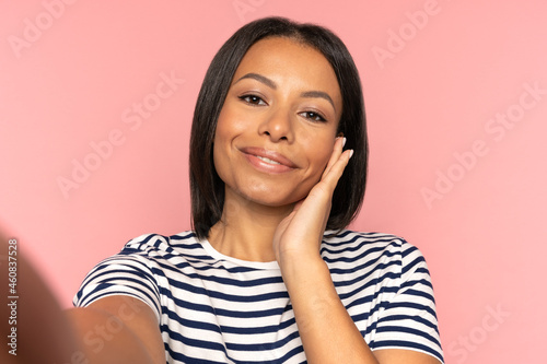 Happy mix race woman taking selfie photo in smartphone camera after skin spa treatment touching perfect face after skincare procedure. Young black girl posing for self portrait shot on cell phone © DimaBerlin