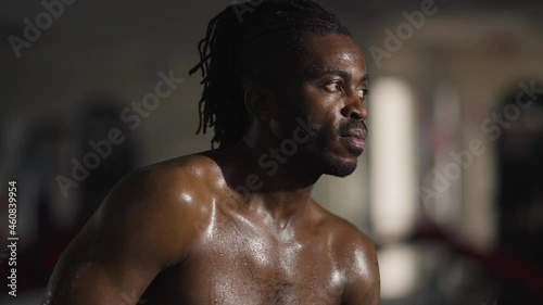Portrait of perspiring African American confident man sitting in gym breathing. Endurant strong handsome sportsman resting working out indoors. Masculinity and healthy lifestyle concept