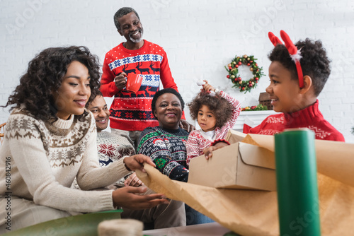 mother and son packing gift box near happy african american family