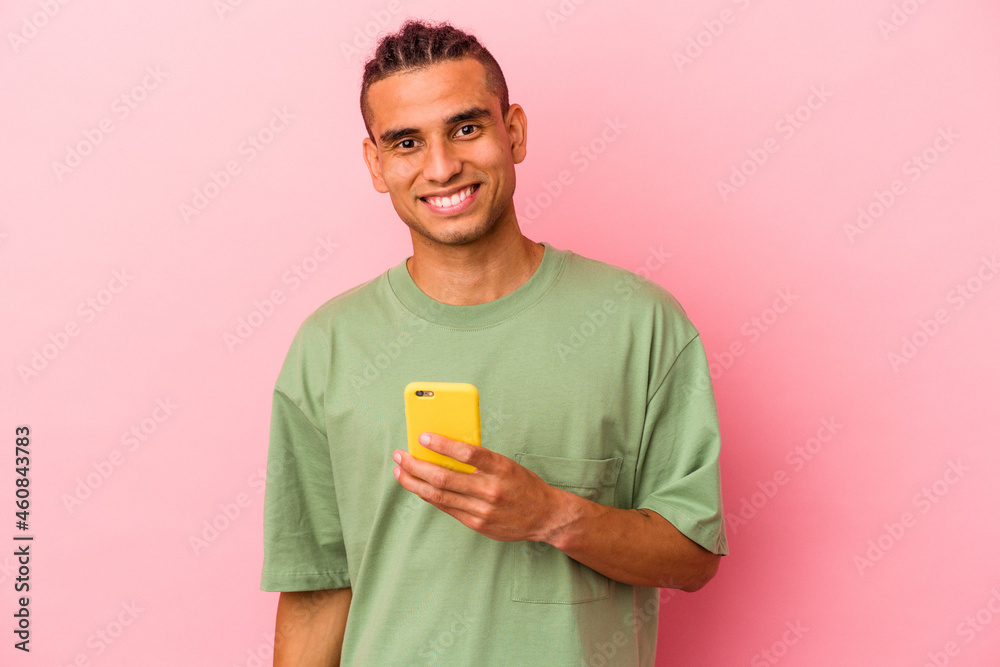 Young Venezuelan man holding a mobile phone isolated on pink background happy, smiling and cheerful. Young Venezuelan man holding a mobile phone isolated on pink background happy, smiling and cheerful.