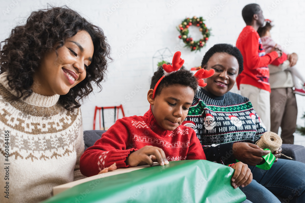african american boy in reindeer horns headband packing christmas present near happy mom and granny african american boy in reindeer horns headband packing christmas present near happy mom and granny