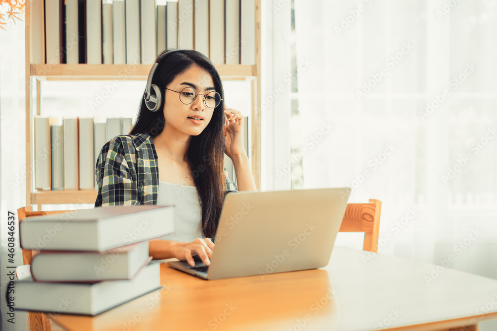 Young female student in plaid shirt sitting at the table using laptop when studying. Young female student in plaid shirt sitting at the table using laptop when studying.