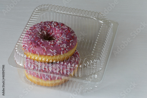 Tasty glazed raspberry donut with topping in a plastic container. Ready for sale. Business concept.