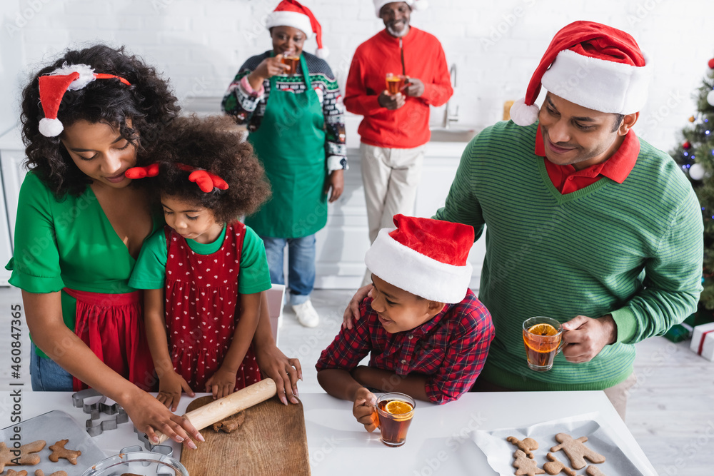 Obraz premium african american woman rolling out dough near family and blurred grandparents drinking orange cinnamon tea