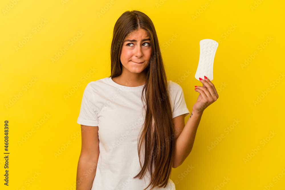 Young caucasian woman holding a compress isolated on yellow background confused, feels doubtful and unsure. Young caucasian woman holding a compress isolated on yellow background confused, feels doubtful and unsure.