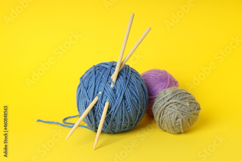 Multi-colored balls of yarn with knitting needles on yellow background
