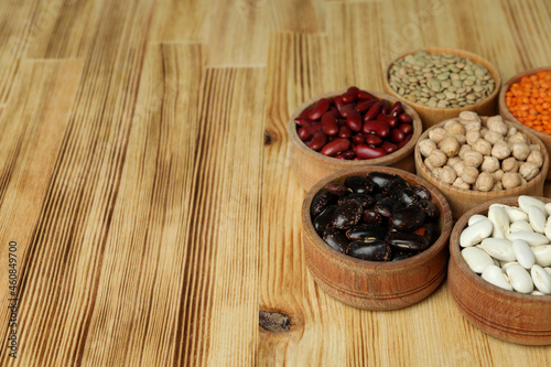 Bowls with different types of beans on a wooden background