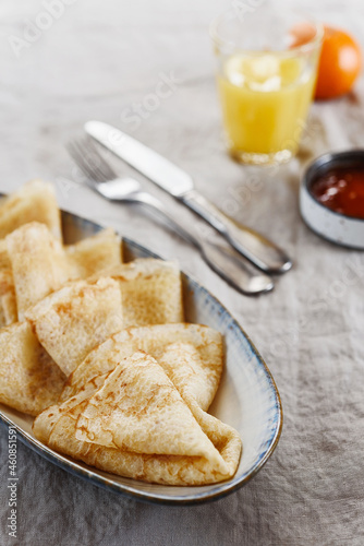 Breakfast with crepes or pancakes and jam, juice and tangerine on greige linen tablecloth. Pancake week or Shrovetide. Selective focus
