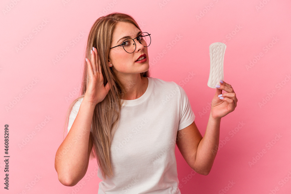 Young russian woman holding a compress isolated on pink background trying to listening a gossip. Young russian woman holding a compress isolated on pink background trying to listening a gossip.