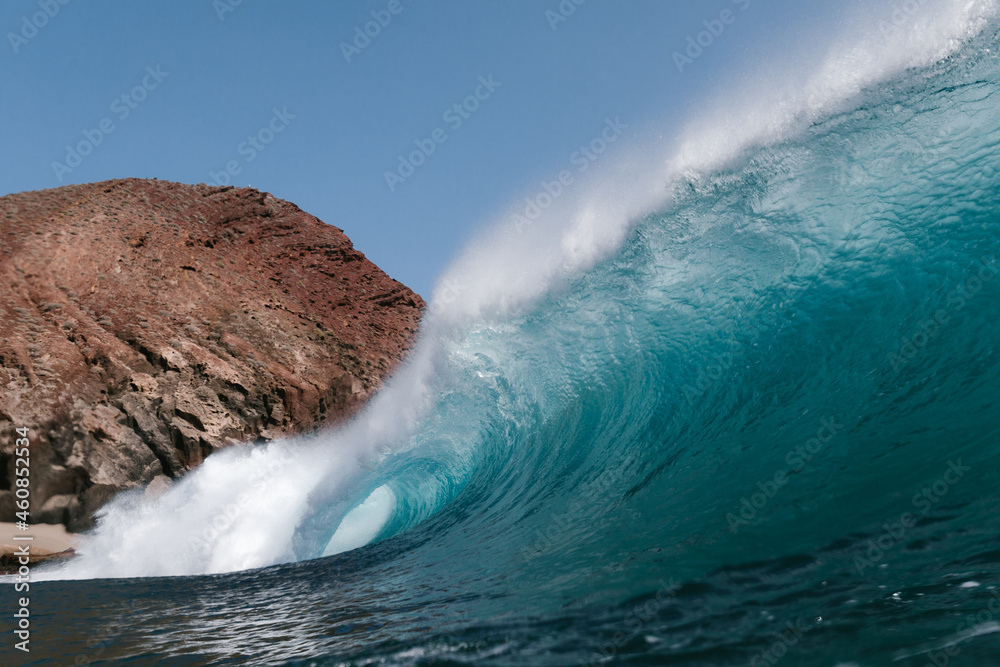 Naklejka premium Blue wave breaking front a red mountain in Tenerife