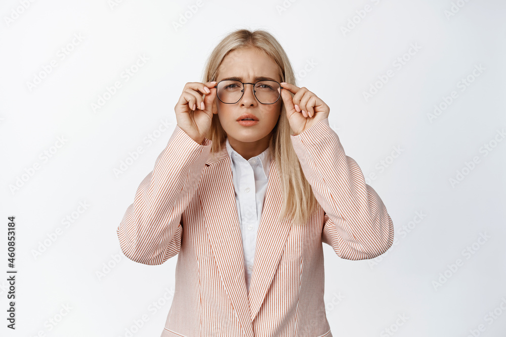 Young businesswoman cant see, looking through glasses with squinting eyes, cant read something, standing over white background - obrazy, fototapety, plakaty 