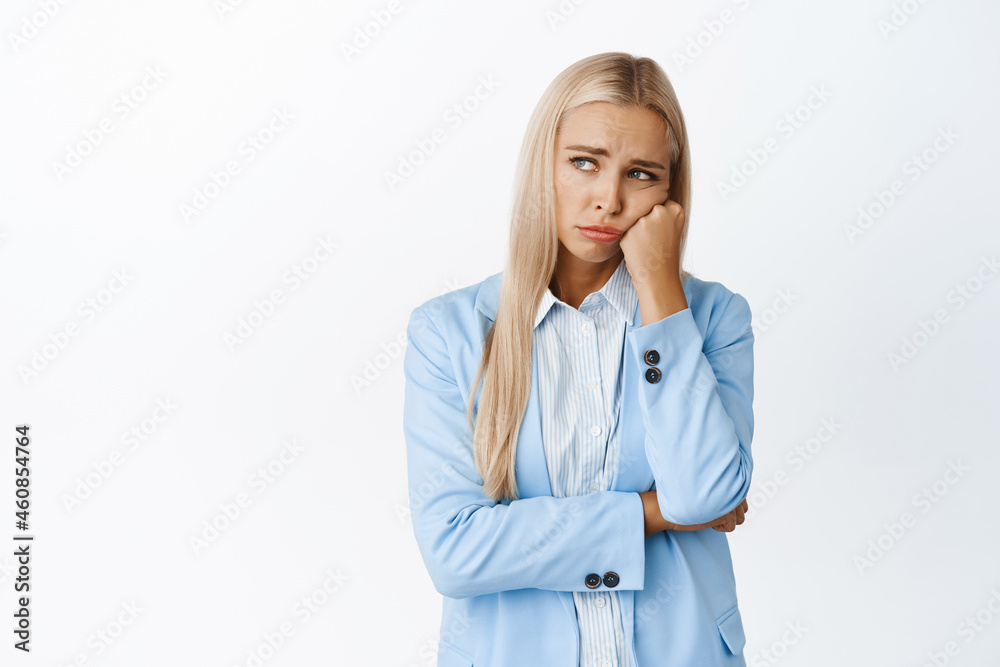 Sad and gloomy young office worker, saleswoman sulking and frowning distressed, standing upset in fancy suit against white background Sad and gloomy young office worker, saleswoman sulking and frowning distressed, standing upset in fancy suit against white background