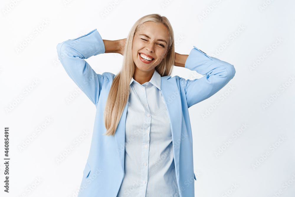 Smiling businesswoman in suit standing relaxed, winking and holding hands behind head in resting pose, white background Smiling businesswoman in suit standing relaxed, winking and holding hands behind head in resting pose, white background