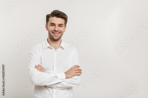 Image of happy smiling brunette man wearing white shirt smiling at camera with hands crossed on chest isolated over white background