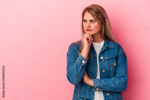 Young russian woman isolated on pink background looking sideways with doubtful and skeptical expression.