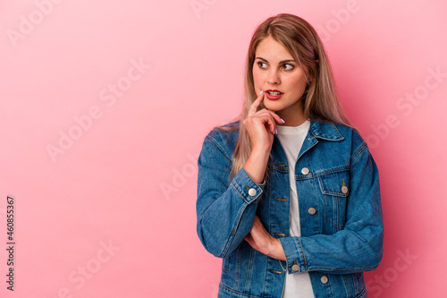 Young russian woman isolated on pink background looking sideways with doubtful and skeptical expression.