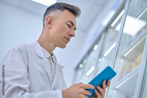 Man in lab coat looking closely at tablet