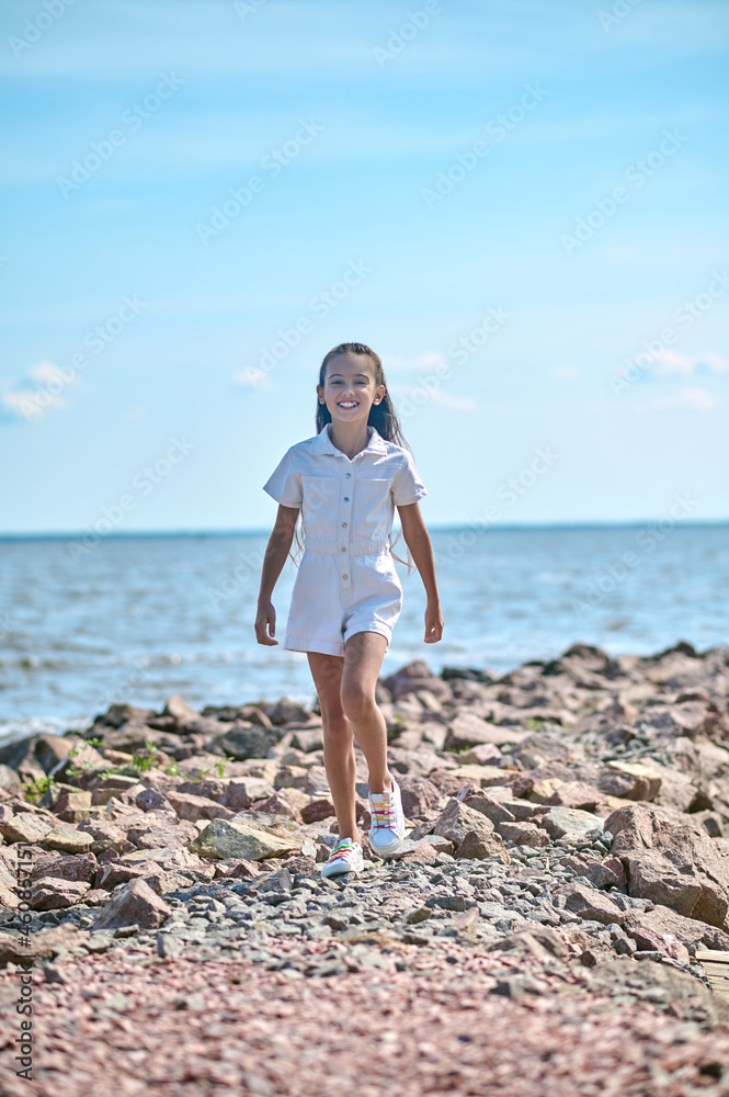 A girl in a white dress walking on a beach
