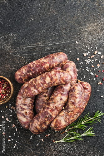 Raw sausages or bratwurst and ingredients for cooking on dark stone background. Top view with copy space.