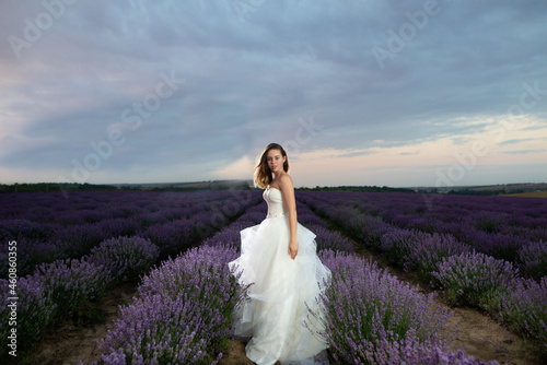 lovely bride on a lavender field in a white wedding dress among flowers. Wedding day among the flowering bushes of lavender in summer at sunrise.