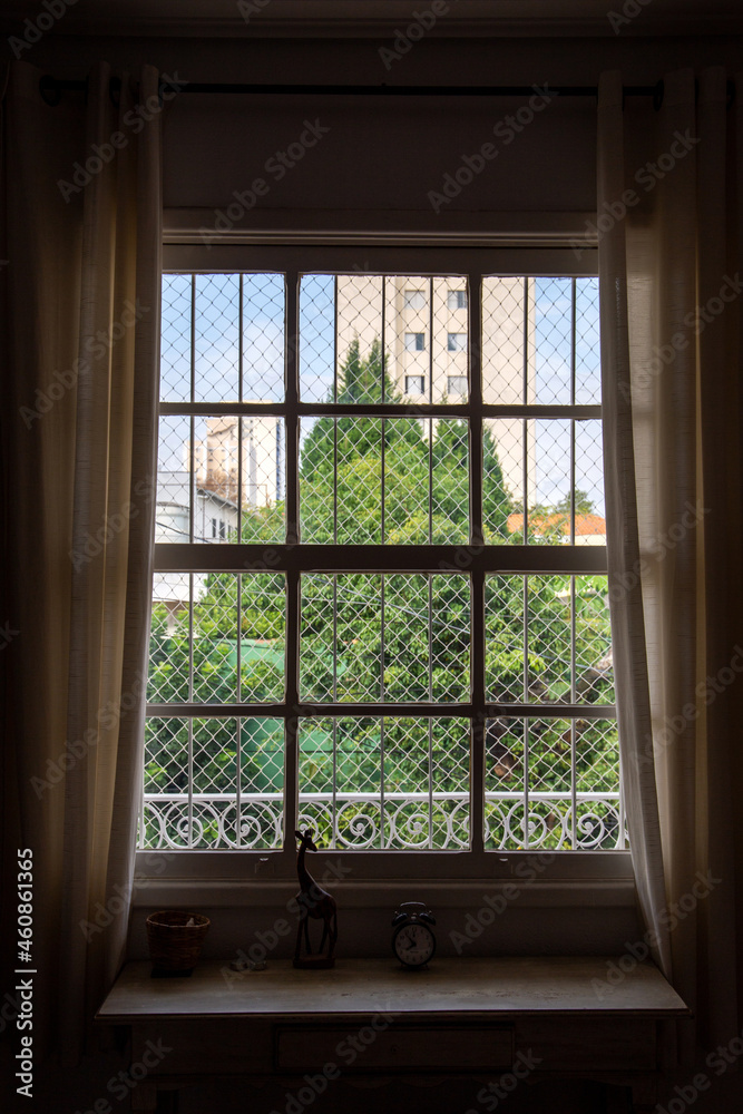 window with grid with home garden background and white curtain. With sideboard furniture and an old clock window with grid with home garden background and white curtain. With sideboard furniture and an old clock