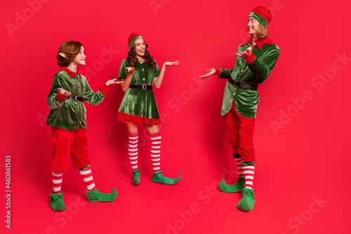 Full size photo of cheerful santa helper talk good mood north-pole celebrate xmas isolated on red color background