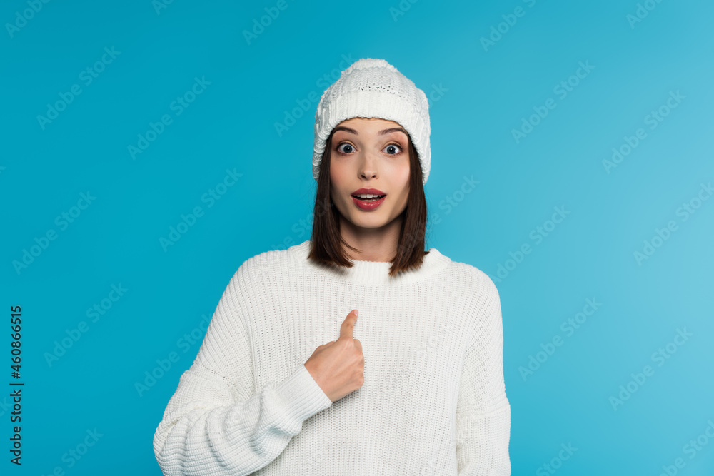 Amazed woman in warm clothes pointing with finger isolated on blue Amazed woman in warm clothes pointing with finger isolated on blue