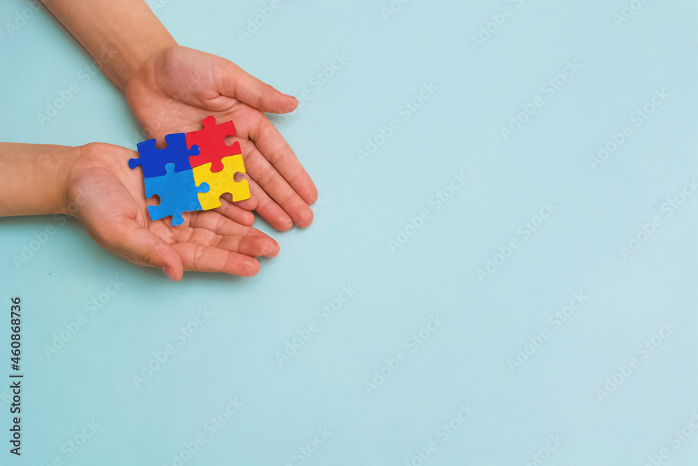 World autism awareness day. The hands of a small child holding colorful puzzles on blue background. Copy space. Banner