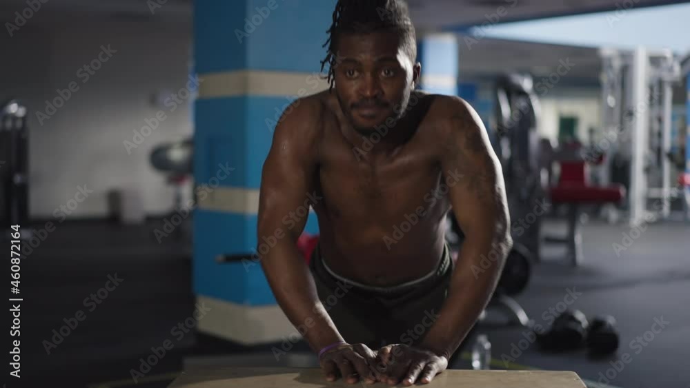 Front view tattooed sweating African American sportsman doing push-ups on gym cube indoors. Portrait of motivated confident man exercising training indoors. Sportive lifestyle concept Front view tattooed sweating African American sportsman doing push-ups on gym cube indoors. Portrait of motivated confident man exercising training indoors. Sportive lifestyle concept