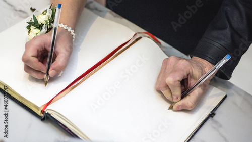 Man and a woman signing a wedding guest book with a pen.