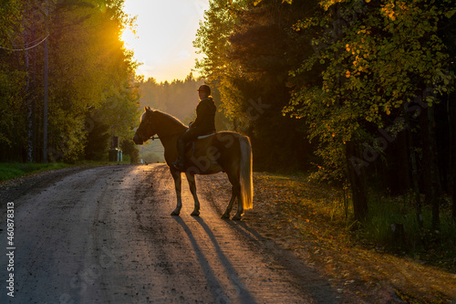 Woman horseback riding on the country road at sunset