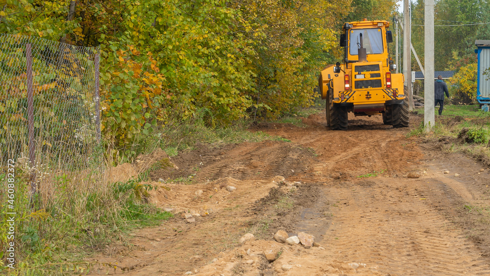 Rural road construction with grader in autumn daytime. The grader repairs the dirt road in the village. Rural road construction with grader in autumn daytime. The grader repairs the dirt road in the village.