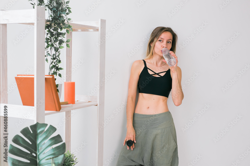 Sporty young woman drinking water after training at home. Active lifestyle and wellness. Sporty young woman drinking water after training at home. Active lifestyle and wellness.
