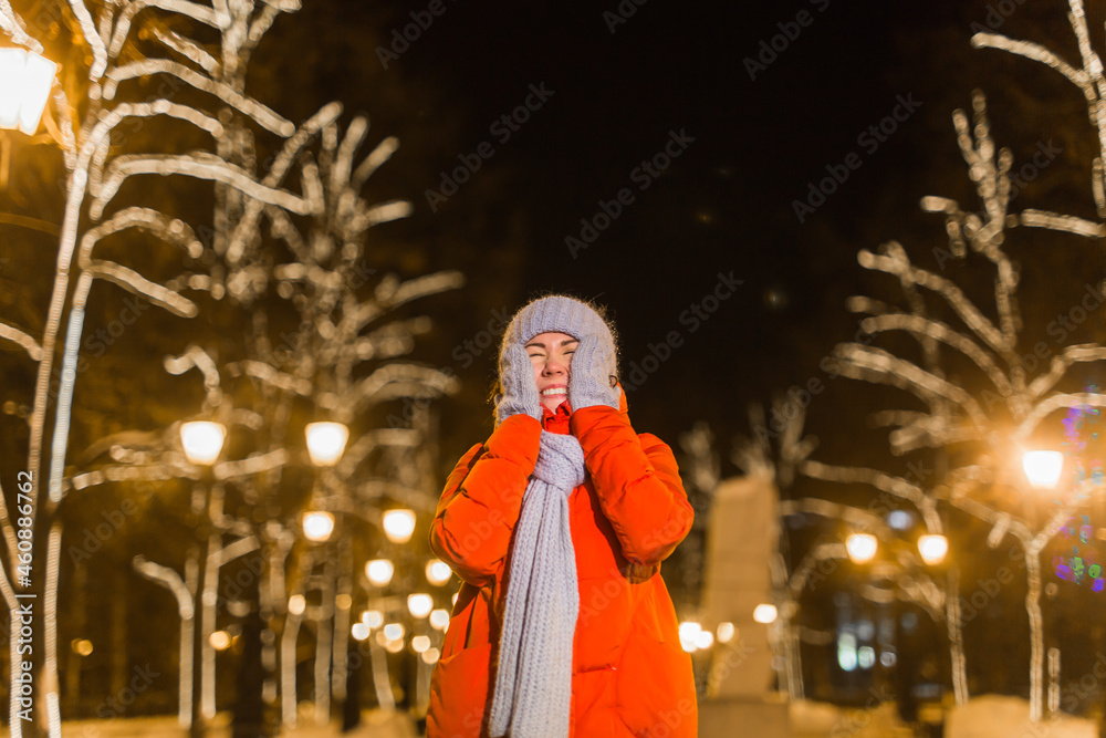 Happy funny young woman with winter clothes background evening city lights illumination. Christmas and winter holidays concept.