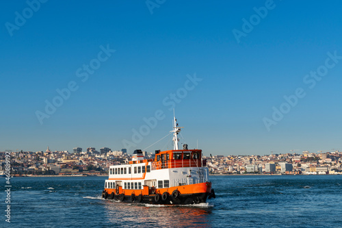 A traditional cacilheiro ferry boat crossing the Tagus River (Rio Tejo) with the city of Lisbon skyline on the background.