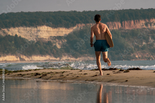 Young sportive man is running with his skimboard on the beach on sunrise