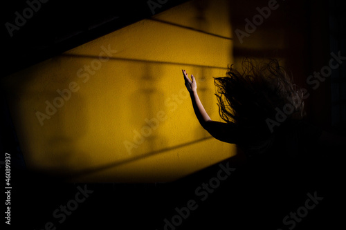 Silhueta de mulher misteriosa com braço pra cima e cabelos esvoaçantes com sombra de uma janela.