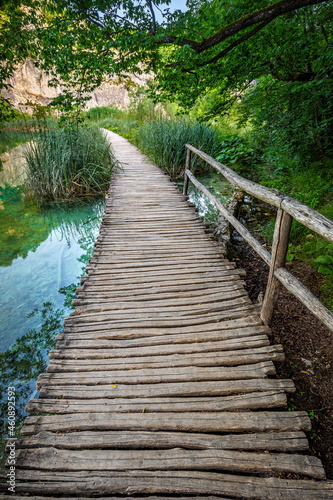 Plitvice  Croatia - Wooden walkway in Plitvice Lakes National Park on a bright summer day with crystal clear turquoise water  small waterfalls and green summer foliage